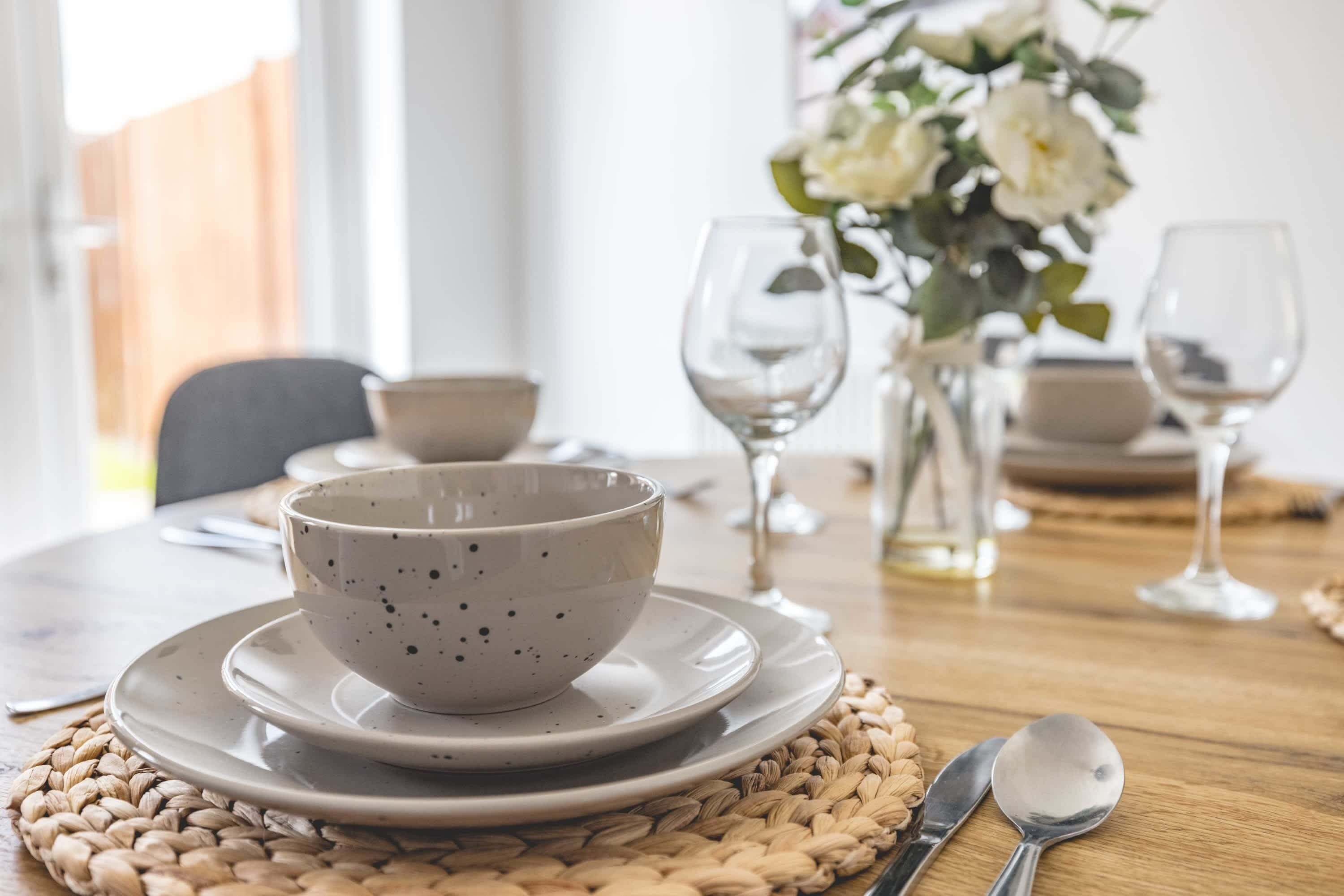A dining table set with plates, bowls, and cutlery, with a woven placemat underneath.