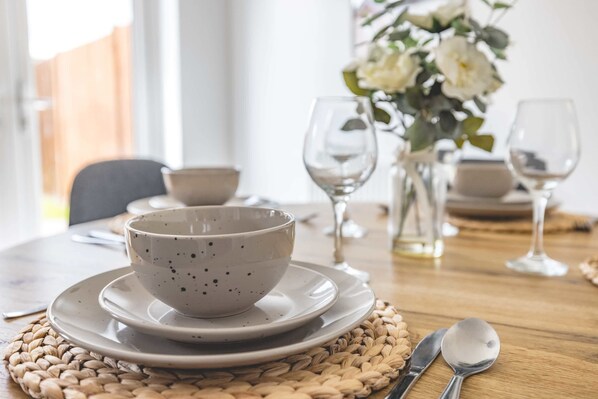 A dining table set with plates, bowls, and cutlery, with a woven placemat underneath.