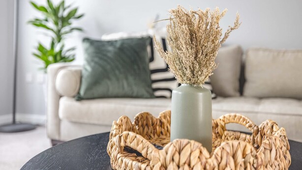 Un salon avec un panier tressé posé sur une table, un vase contenant des fleurs séchées, une plante verte et un canapé à rayures.