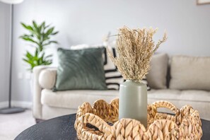 A living room with a woven basket on a table, a vase with dried flowers, a green plant, and a striped couch.