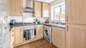Une cuisine moderne avec des meubles en bois, un four encastré, un lave-linge et une fenêtre qui laisse entrer la lumière naturelle.