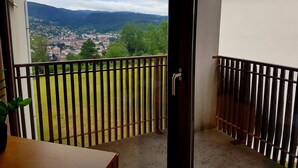 A balcony with a metal railing, a door, and a view of a town and mountains. - The DRYADES Mountain view (Gérardmer)
