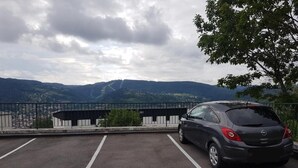 A parking area with marked spaces, a car, and a view of distant hills and a building. - The DRYADES Mountain view (Gérardmer)