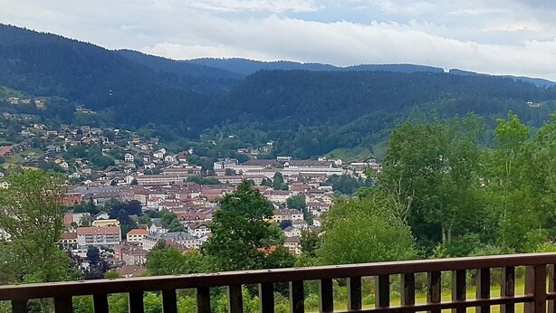 A town with a mix of residential and commercial buildings, surrounded by hills and greenery. - The DRYADES Mountain view (Gérardmer)