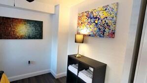 A modern living room with a large abstract painting, a black console table with a lamp, and a dark wood floor.