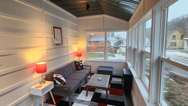 A cozy room with a sofa, two side tables with lamps, a small table, and a view of a snowy landscape through large windows.