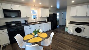 A modern kitchen with white cabinets, a black stove, a microwave, and a washing machine.