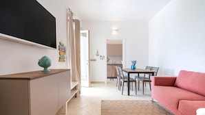 A living room with a sofa, a TV, a dining area with chairs and a table, and a kitchen in the background. - Holiday Apartment "Villa Katia - Villanova di Ostuni" with Private Terrace and Wi-Fi (Villanova di Ostuni)