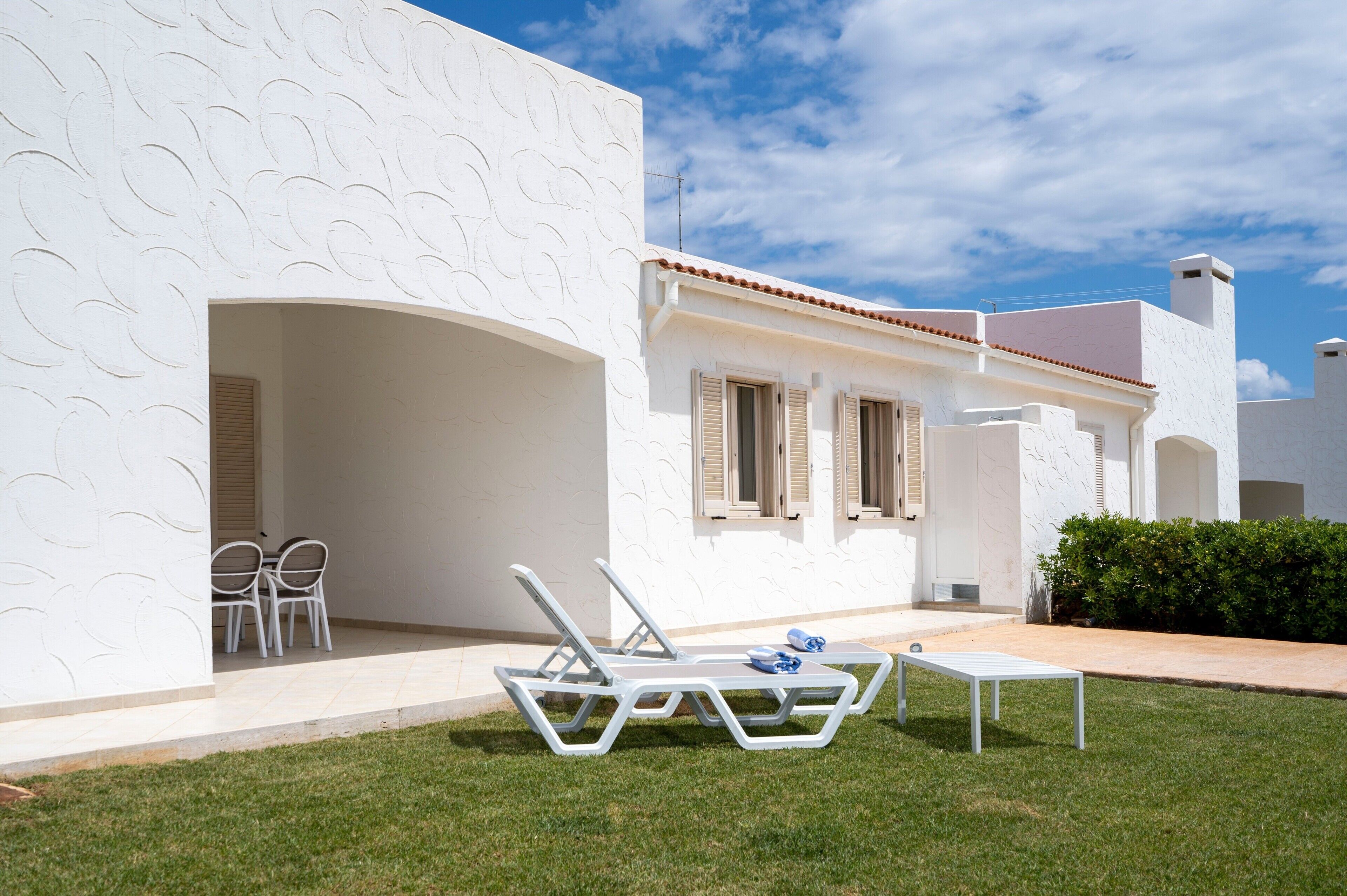 Un edificio blanco con un patio, que incluye una mesa y dos sillones.