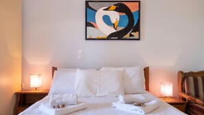 A hotel room with a bed, two bedside lamps, a painting of swans, and a wooden headboard. - Apartment "Apollon" with Sea View, Garden & Wi-Fi (Lefkada)