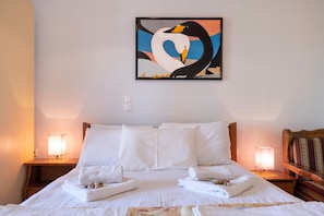 A hotel room with a bed, two bedside lamps, a painting of swans, and a wooden headboard.