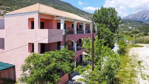 A pink building with a tiled roof, multiple balconies, and a view of a mountainous landscape. - Apartment "Apollon" with Sea View, Garden & Wi-Fi (Lefkada)