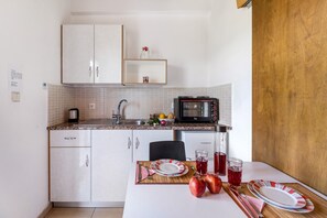 A kitchen with white cabinets, a microwave, a sink, and a dining table set with plates, cutlery, and apples.