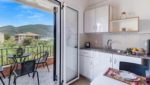A balcony with a table and chairs, a kitchen with cabinets and a countertop, and a view of a mountainous landscape. - Apartment "Studio Rea" with Sea View, Garden & Wi-Fi (Lefkada)