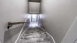 Un escalier étroit et droit, muni d’une main courante sur le côté gauche, mène à une porte située en haut.