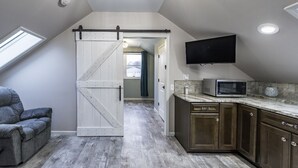 Une cuisine de style industriel, avec une porte coulissante de type grange, un téléviseur à écran plat et un four à micro-ondes posé sur le plan de travail.