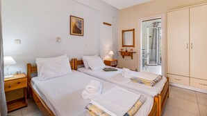 Une chambre d’hôtel avec deux lits, une armoire, une table de chevet avec une lampe, un tableau encadré au mur et une vue sur l’extérieur.