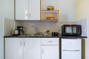 A compact kitchen with white cabinets, a coffee maker, a microwave, and a small refrigerator.
