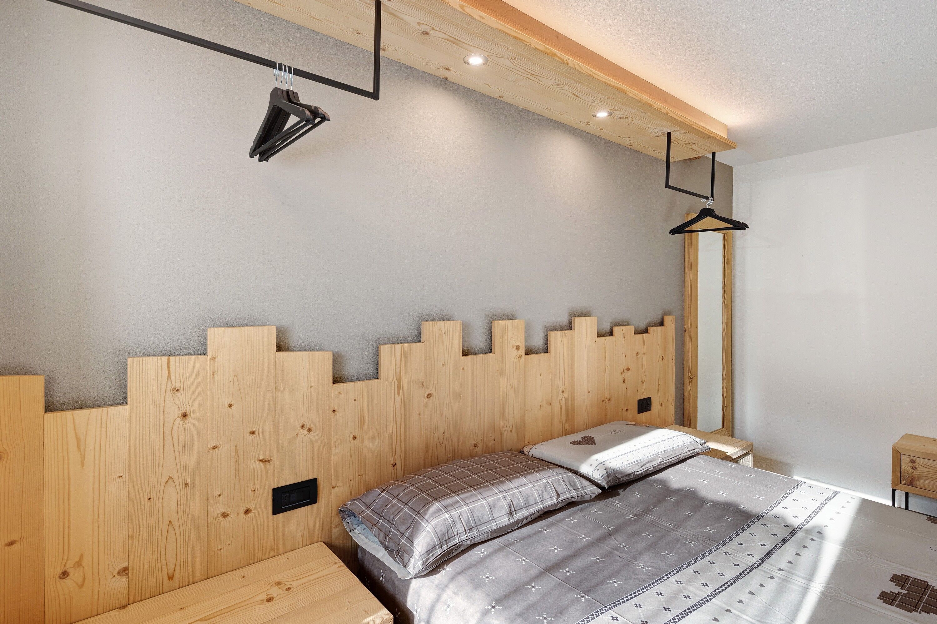 Une chambre à coucher avec une tête de lit en bois, un lit recouvert d’une literie à motifs, une table de chevet et un luminaire suspendu.