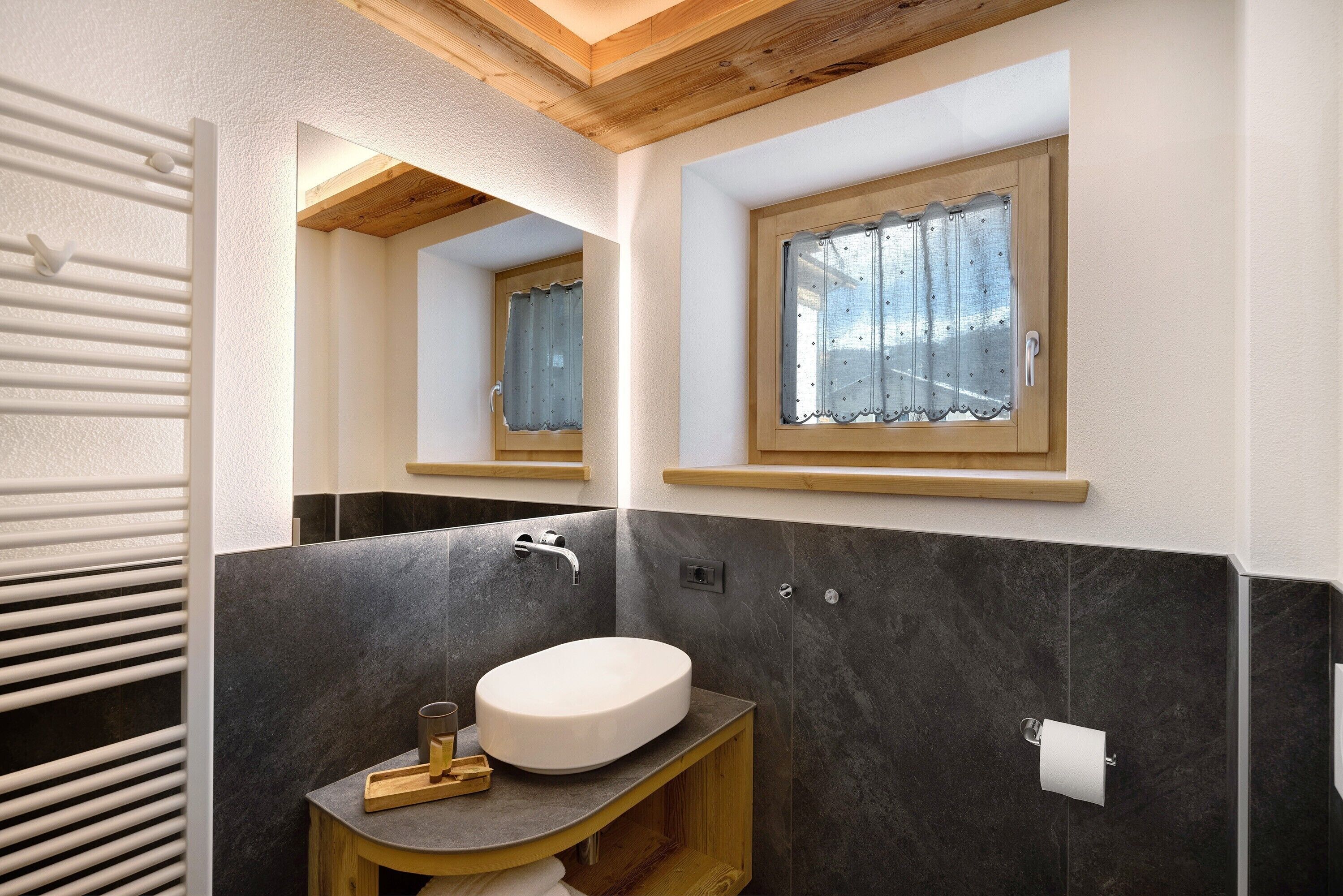A bathroom with a wooden vanity, a sink, a mirror, a window with a curtain, and a towel rack.