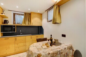 Una cocina compacta con armarios de madera, microondas y una mesa de comedor con mantel estampado.