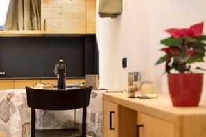 Un coin repas avec une table dressée pour deux personnes, une chaise, une bouteille de vin et une plante en pot.