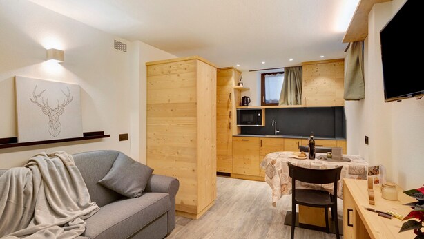 A compact living space with a sofa, a dining table, a kitchen area, and a television. - Apartment "Stelo Rosina's Home" (Livigno)