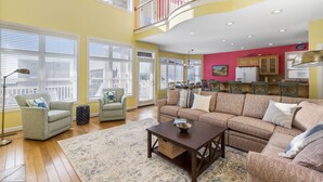 A spacious living room with a large sectional sofa, a coffee table, and a floor lamp. There are two armchairs and a rug on the wooden floor. - Makin' Memories! Clean, Comfortable, and Enjoyable! (Ocean Isle Beach)