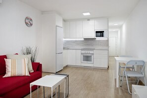 Une cuisine moderne avec des meubles blancs, un four à micro-ondes et une cuisinière. On y trouve un canapé rouge avec des coussins à rayures et une petite table.