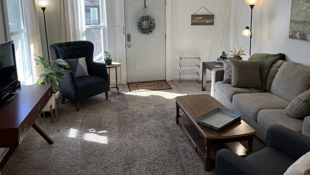 Una sala de estar con un sillón oscuro, un sofá, una mesita de centro y un televisor sobre un mueble de madera.