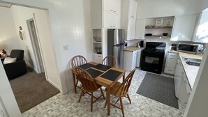 Una cocina compacta con armarios blancos, una estufa negra y un microondas. Hay una mesa de comedor con cuatro sillas.