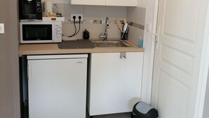Uma cozinha compacta com micro-ondas, pequena geladeira, pia e lixeira.