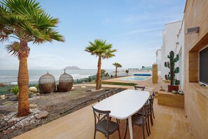 A patio with a table and chairs, palm trees, a cactus, and a pool.