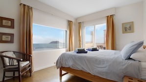 A bedroom with a bed, a chair, a window with curtains, and a view of the sea. - Holiday Home "Ocean Spirit" Near Beach with Sea View, Pool & Wi-Fi (Corralejo)