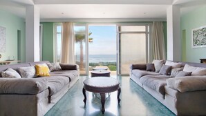 A spacious living room with two sofas, a round coffee table, and a large sliding glass door leading to a balcony with a view of the ocean. - Holiday Home "Ocean Spirit" Near Beach with Sea View, Pool & Wi-Fi (Corralejo)