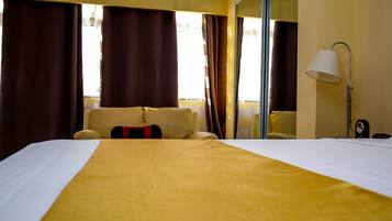 Una habitación de hotel con una cama grande, una mesita de noche, una lámpara y vistas al exterior a través de la ventana.