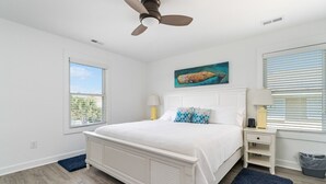 A bedroom with a white bed, a ceiling fan, a painting, a nightstand, and a window with blinds. - Impeccable home w/ pool on the desirable Ocean Ridge Drive of Atlantic Beach, NC (Atlantic Beach)