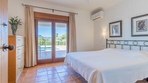 Ein Schlafzimmer mit Bett, Deckenventilator, Blick auf einen Pool und einer Tür mit Pflanze.