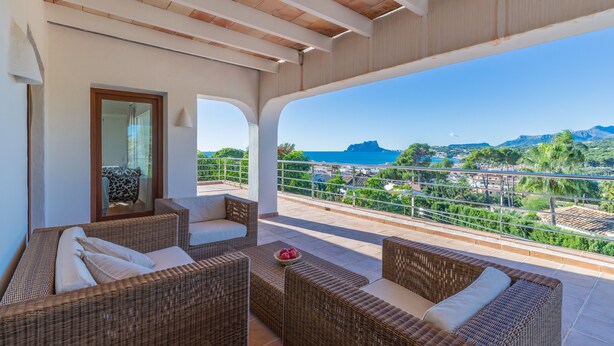 Ein Balkon mit Korbmöbeln, Blick auf das Meer und ein Berg in der Ferne.
