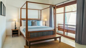 Un lit à baldaquin avec un cadre en bois, deux tables de chevet avec des lampes, un banc au pied du lit et une grande porte-fenêtre coulissante donnant sur un espace extérieur.