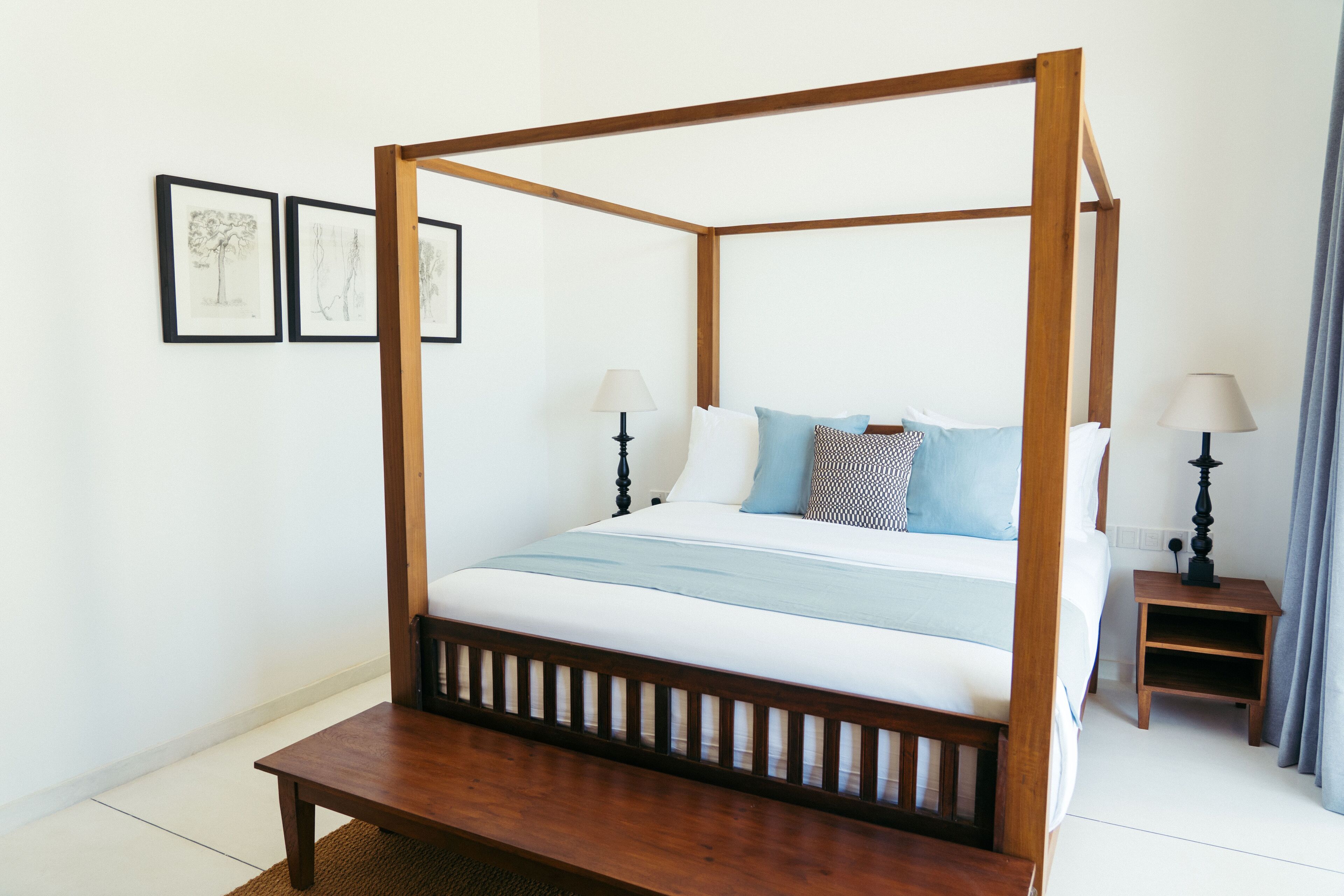 A four-poster bed with a wooden frame, white bedding, and two bedside tables with lamps.