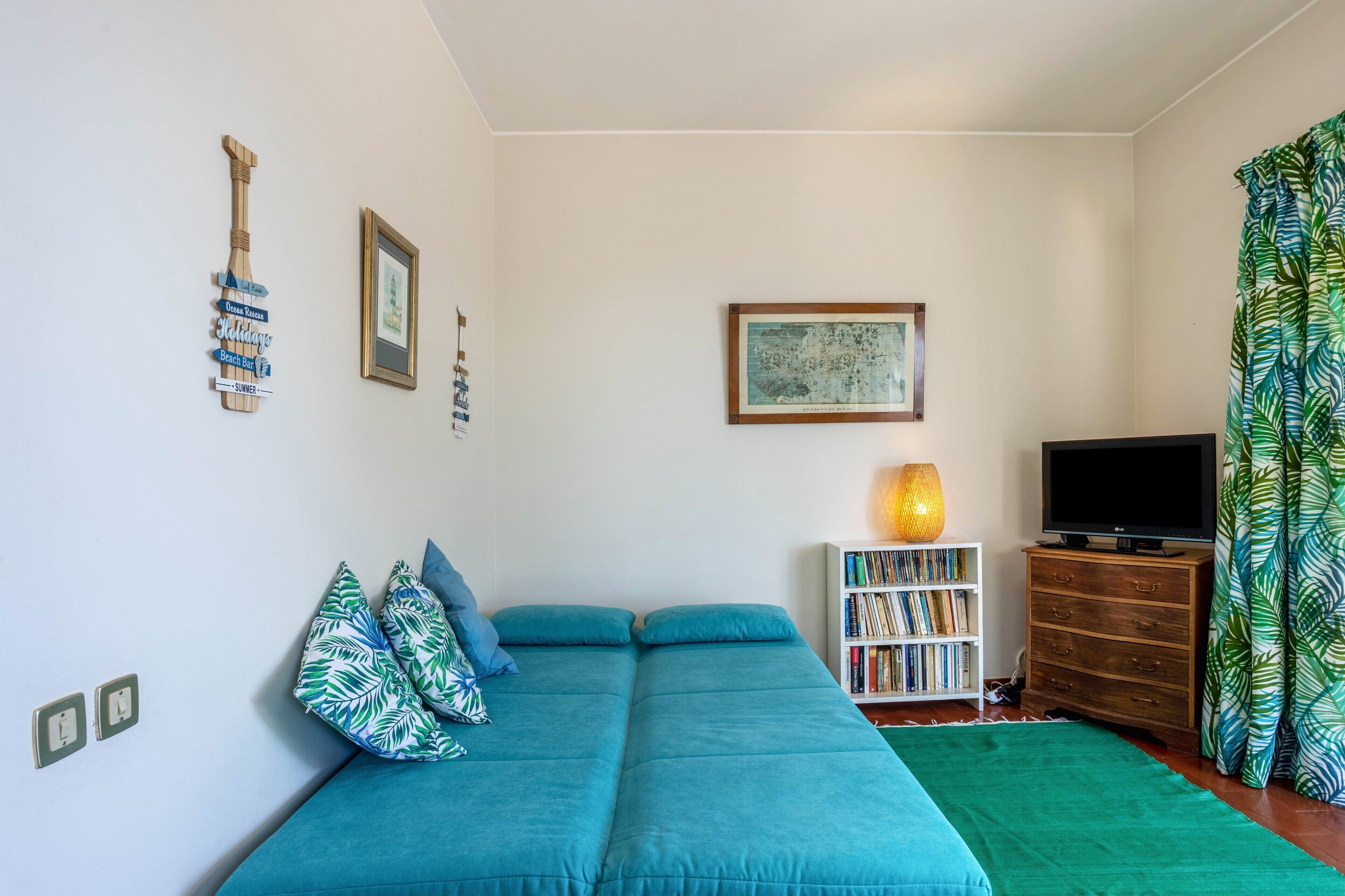 A room with a teal sofa, a bookshelf, a framed picture, and a television.