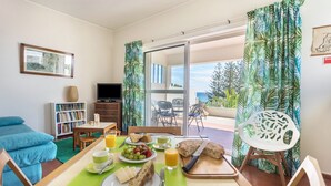 A dining area with a table set for breakfast, a sofa, a bookshelf, and a TV. - Holiday Home "Formosa Beach" with Sea View, Terraces & Wi-Fi (Porto Santo)