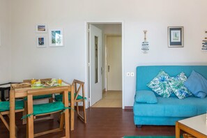 A room with a blue sofa, a wooden dining table with chairs, and a door leading to another room. - Holiday Home "Formosa Beach" with Sea View, Terraces & Wi-Fi (Porto Santo)