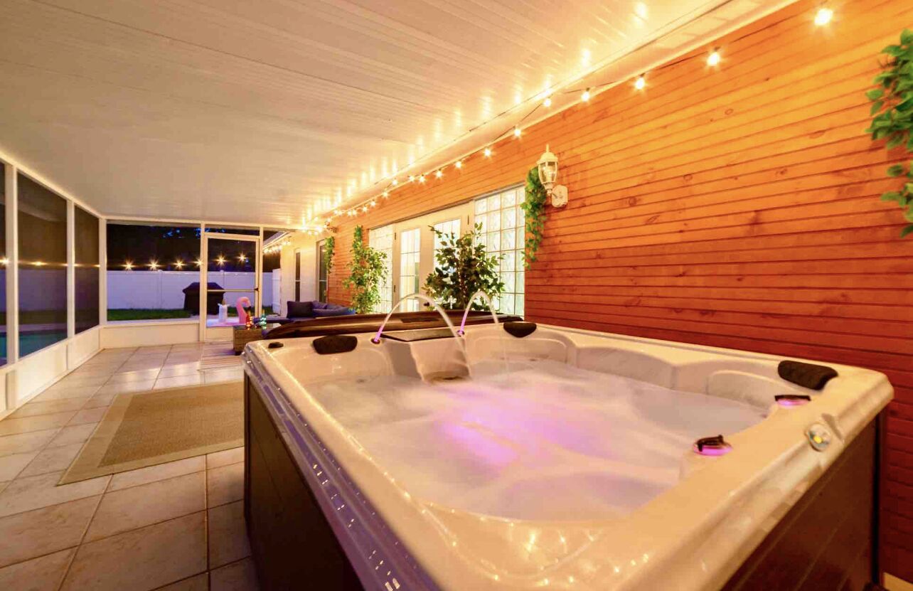 Ein Whirlpool mit Holzwand, Lichterkette, einem Fenster und Blick auf einen Pool.