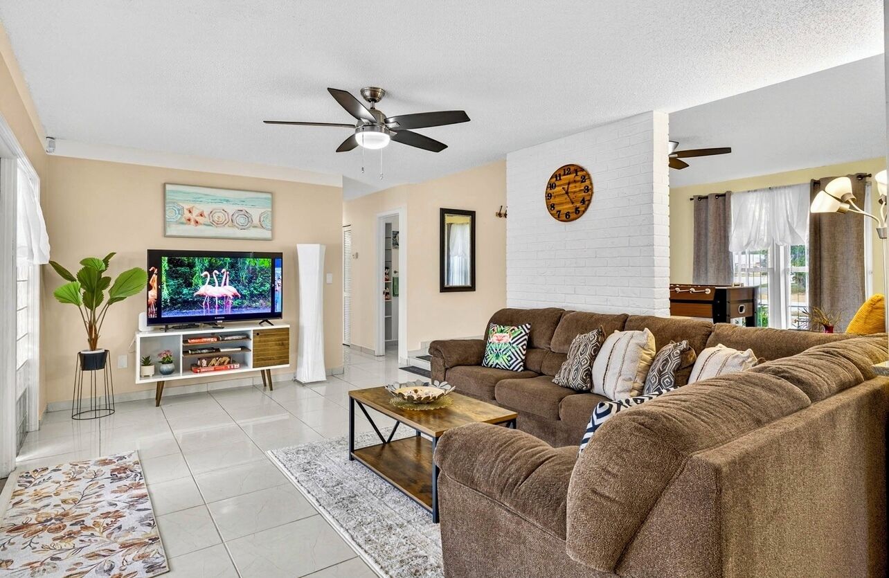 A living room with a sofa, coffee table, TV, ceiling fan, and a clock on the wall.