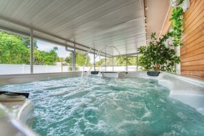 A hot tub with a wooden deck and a potted plant.