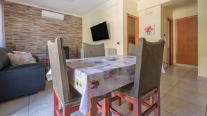 Un coin repas avec une table dressée pour quatre personnes, un canapé, un téléviseur à écran plat fixé au mur et, au fond, une porte en bois.