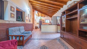 A living room with a sofa, a red chair, a wooden cabinet, and a kitchen area in the background. - Holiday Home "Villa Gabri" with Pool, Garden & Terrace (Carlentini)