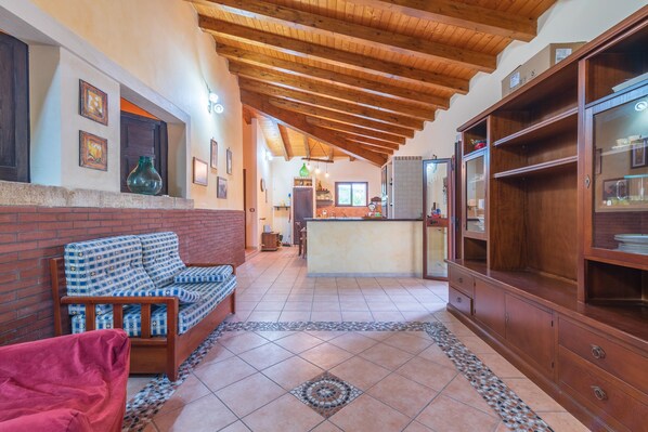 Una sala de estar con un sofá, una silla roja, un aparador de madera y una zona de cocina al fondo.